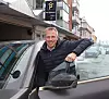 Mann som åpner bildøren i bygate ved parkeringshus